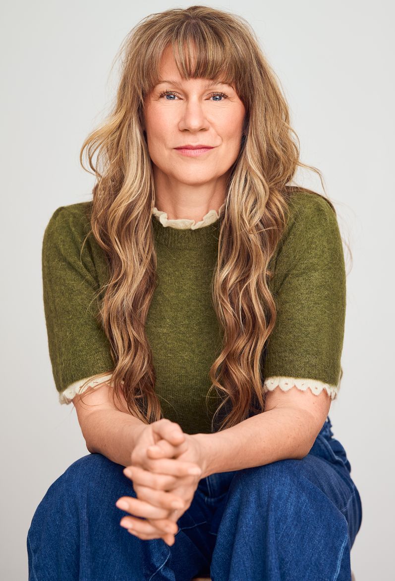 Femme aux cheveux longs, pull vert, regard confiant.